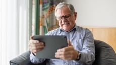 Person sitting in a chair looking at a tablet and smiling