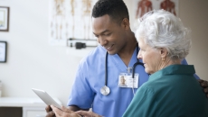 A nurse helping a senior patient use a digital tablet