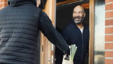 Person answering their front door and getting a delivery from another person