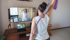 A woman doing exercises guided by a physical therapist on her screen