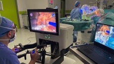 A surgeon operating while other clinicians follow along on a laptop using Proximie's platform