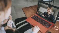 Two individuals sitting on a couch looking at a computer that is on a coffee table with a healthcare professional on the screen