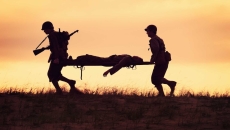 Two soldiers carrying another soldier on a gurney across a field