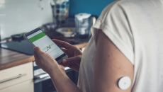 A close up of a person wearing a CGM while tracking glucose levels on their phone