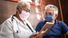 A doctor talking to a patient while holding a tablet.