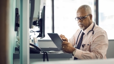 A doctor sitting at his desk using a tablet