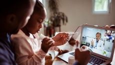 A father and daughter talking to a provider via a video visit on their laptop