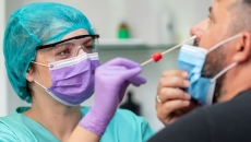Female doctor in protective workwear taking nose swab test from middle aged man wearing protective face mask