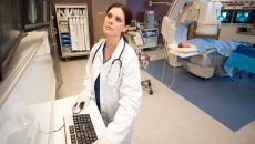 A medical professional looks at images while a patient receives a CT scan in the background