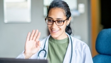Healthcare provider sitting in front of a computer waving at the screen