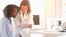 Healthcare provider standing over a patient sitting down while showing them a tablet