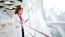 Healthcare provider standing in a hallway looking at a tablet next to a giant window
