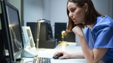 Healthcare provider sitting at a desk looking at a screen with their hand on the mouse