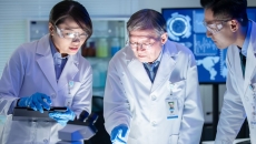 Three healthcare professionals in lab coats looking at something under a light
