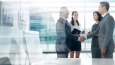 Two people standing in a room shaking hands while two other people stand by them and watch