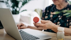 A close up of a person holding a pill bottle while using a laptop