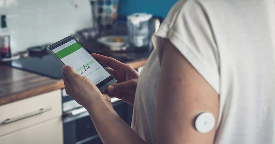 Person wearing a continuous glucose monitor and looking at a phone