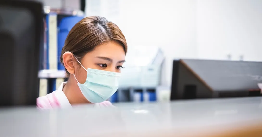 A nurse wearing a surgical mask working at reception