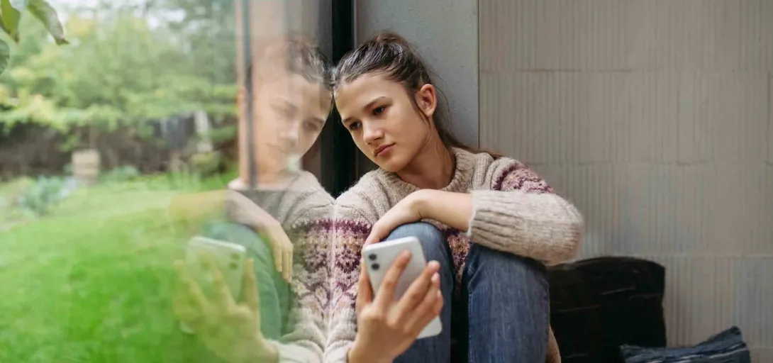 Person sitting by a window while holding a phone
