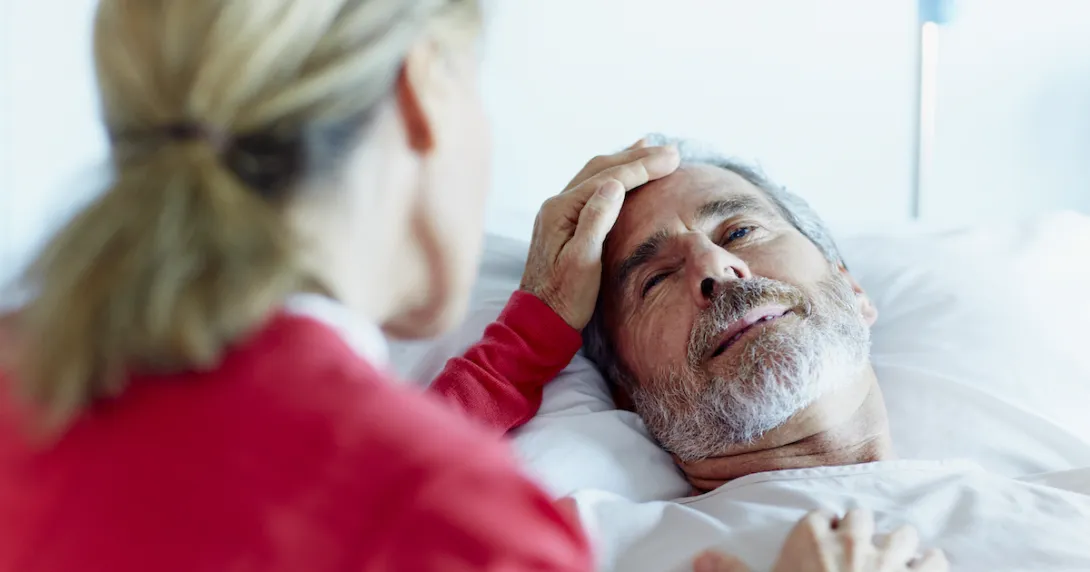 Person in a red shirt sitting next to someone in a hospital gown lying in a bed