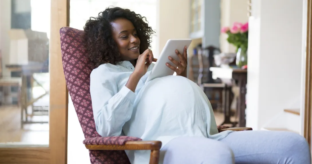 Pregnant person sitting in a chair, looking at a tablet