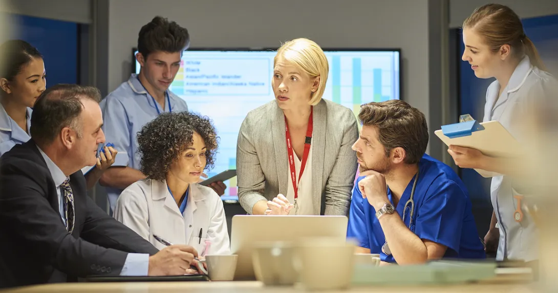 People standing and sitting around a table with a screen showing a graph behind them