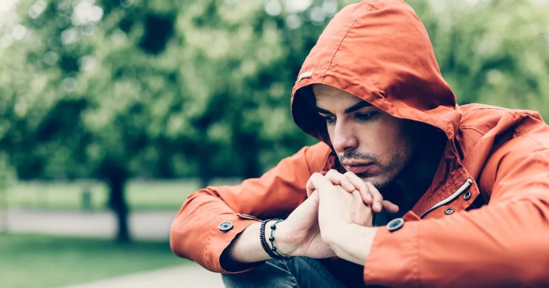 Person sitting in a park while wearing an orange sweater with a hood