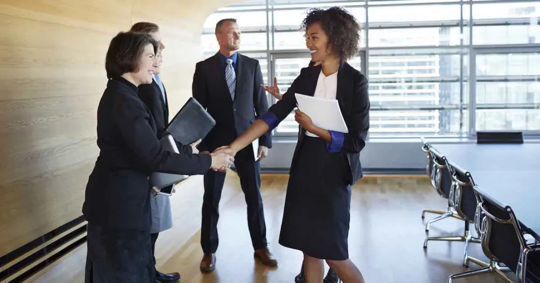 Four business people standing in a room with two of them shaking hands