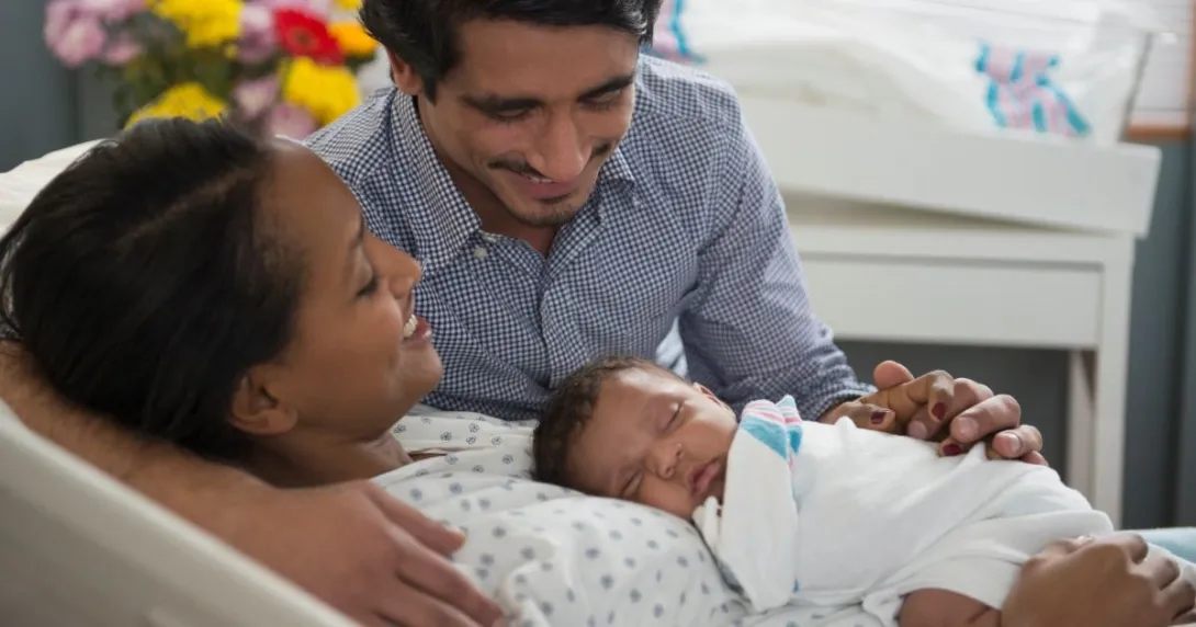 Parents hold infant, one sitting, one laying down