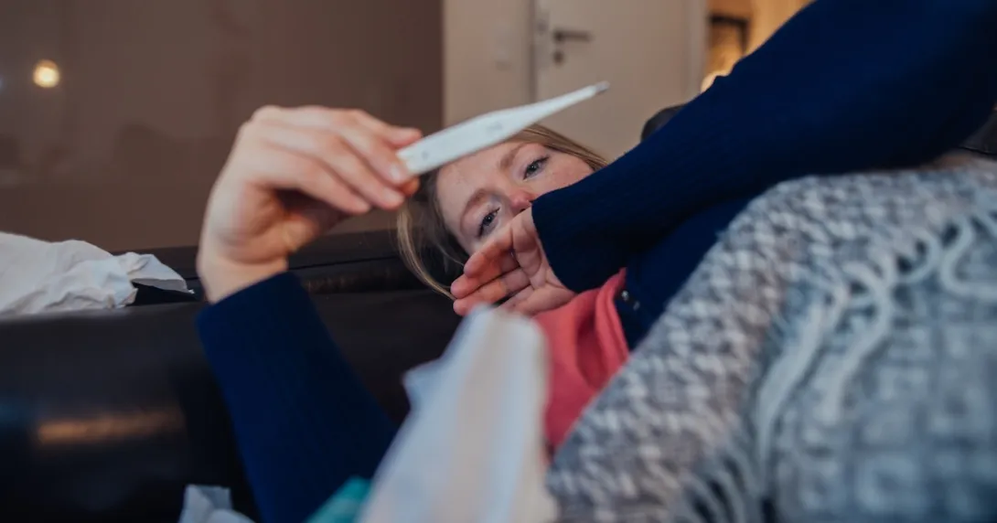 Person lying on their couch looking at a thermometer