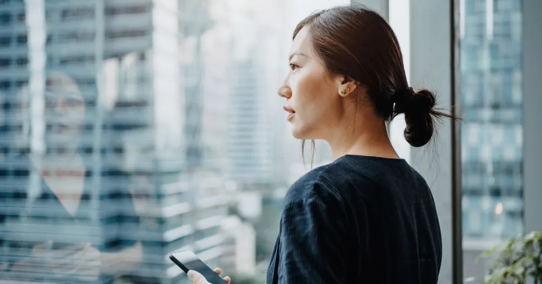 A person holding a smartphone looks out a window