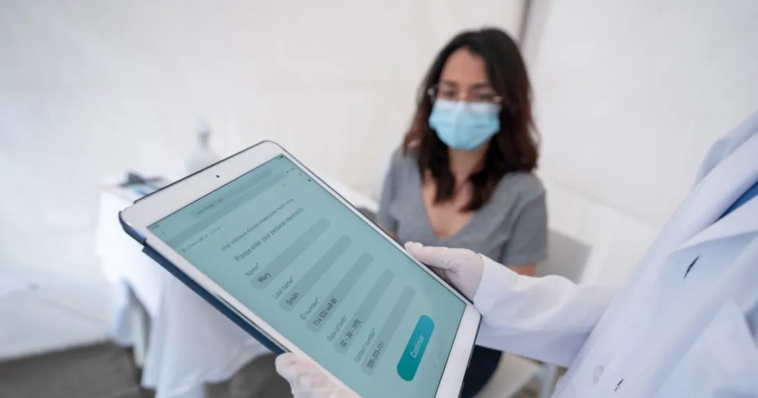Person holding tablet in front of person wearing surgical mask