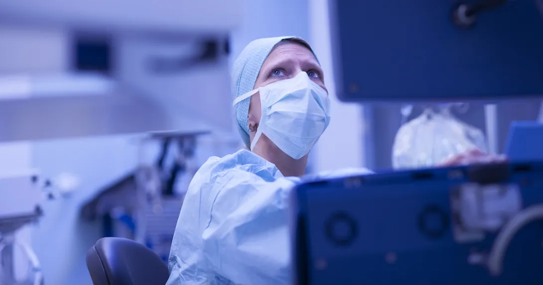 Healthcare provider wearing scrubs and a face mask while looking at a computer screen