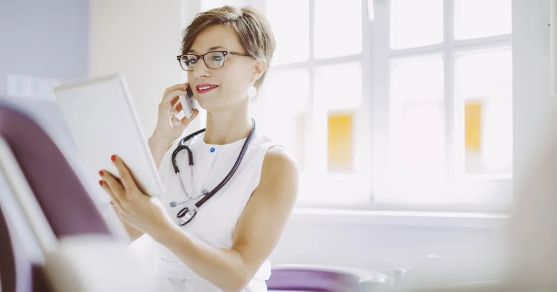 Healthcare provider sitting down in a clinicak setting while looking at a tablet