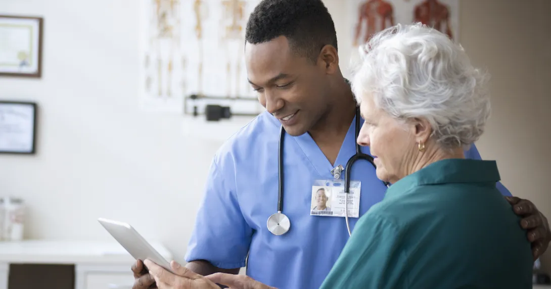 Healthcare professional standing next to a patient while holding a tablet