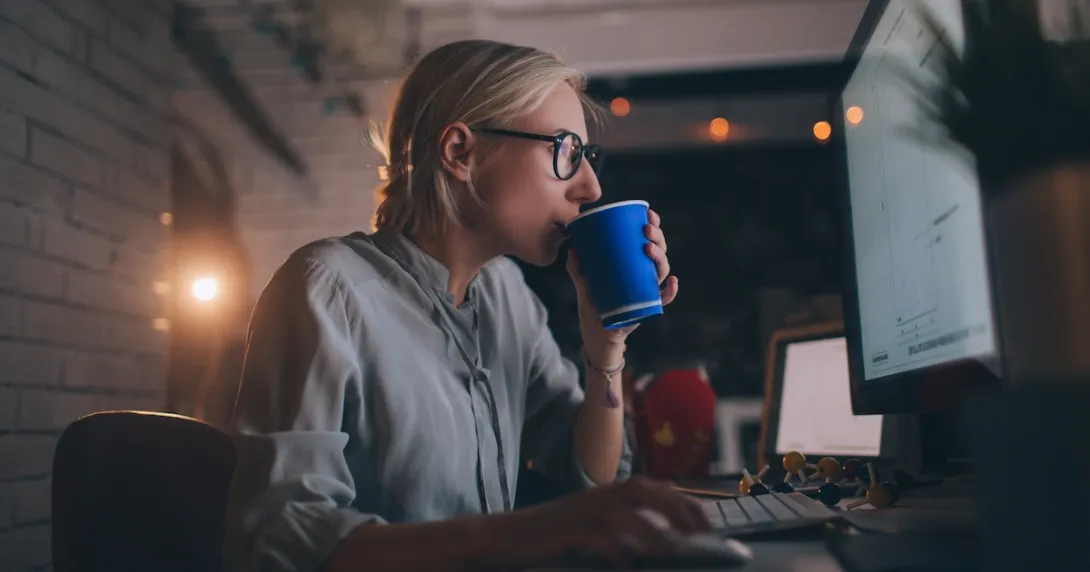 Person sitting at their computer drinking something out of a coffee cup