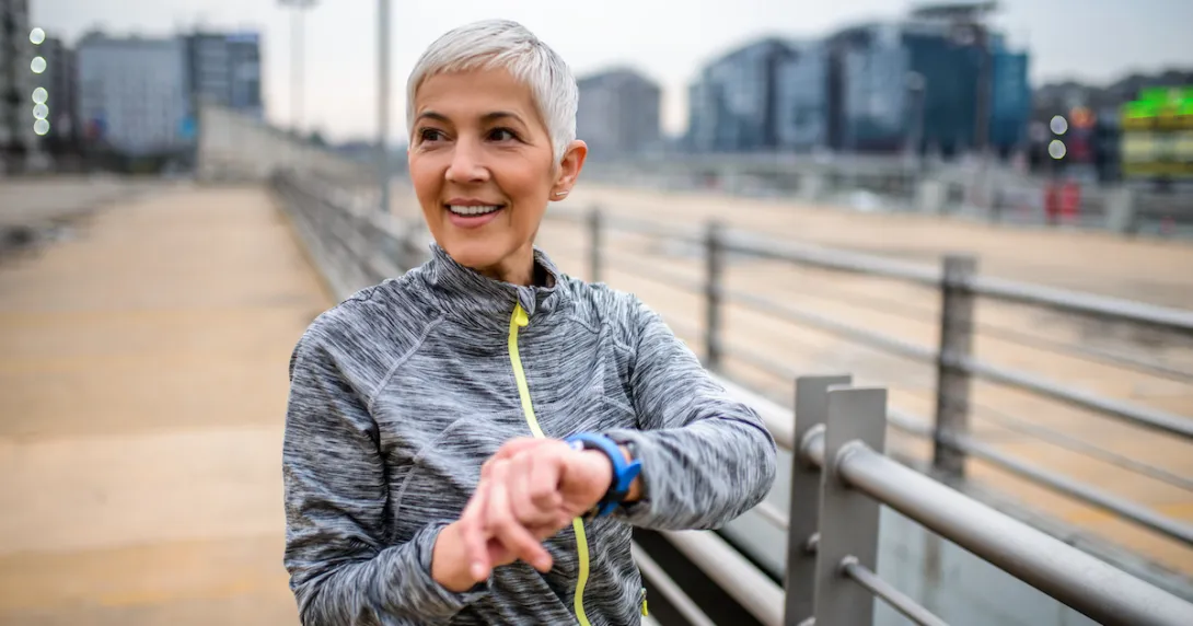 Person standing on a boardwalk holding up their arm while looking at a device on their wrist
