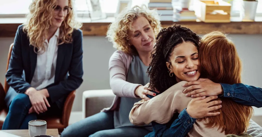 Group therapy session with four people sitting in chairs and two of of them hugging each other