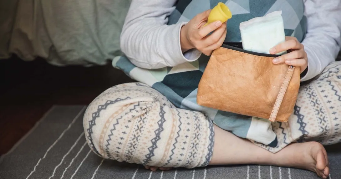 Person pulling period cup and pad out of a brown leather bag