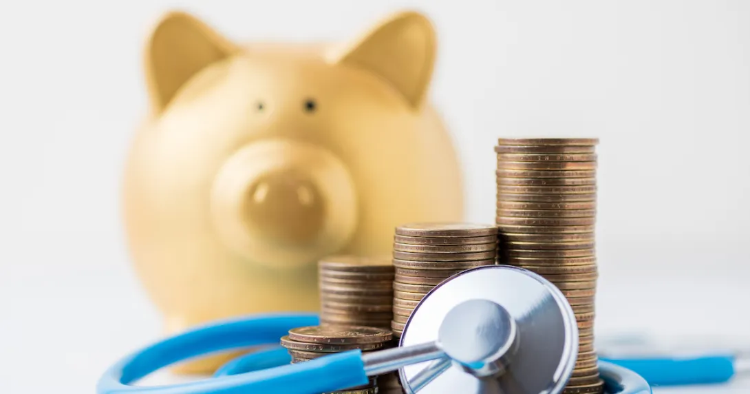 A piggy bank next to a pile of coins and a stethoscope