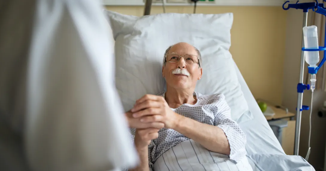 Senior patient holds the hand of a caregiver in hospital bed