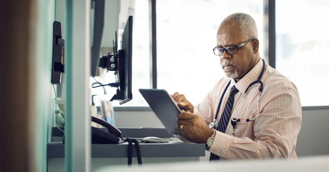 A doctor sitting at his desk using a tablet
