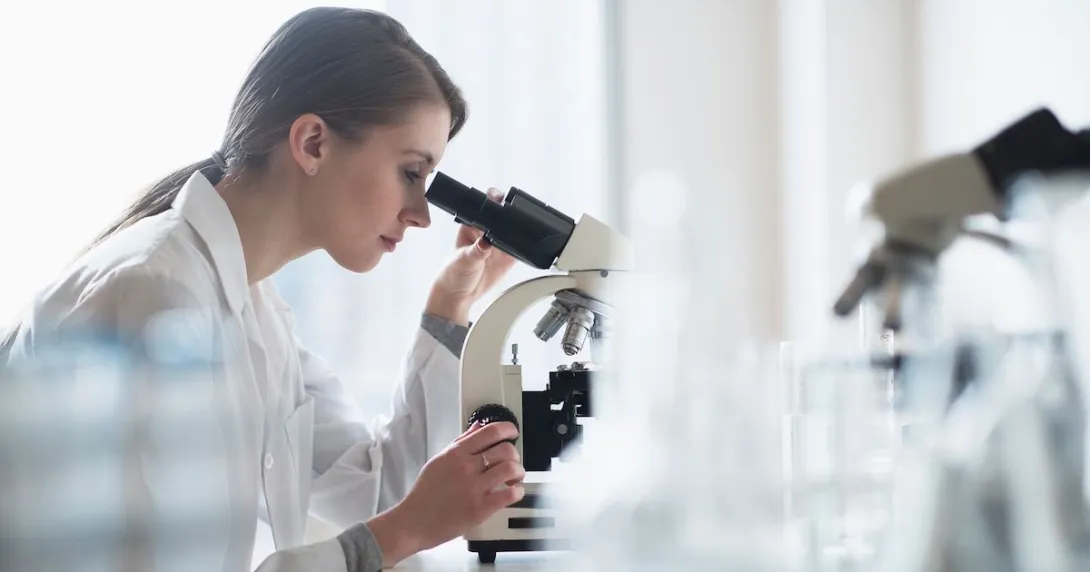 A lab technician analyzing a sample through a microscope