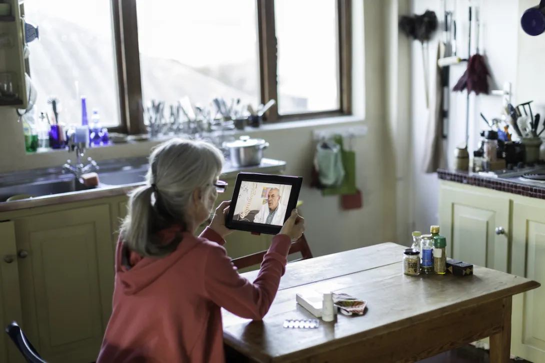 A woman using a tablet to talk to a provider at her kitchen table