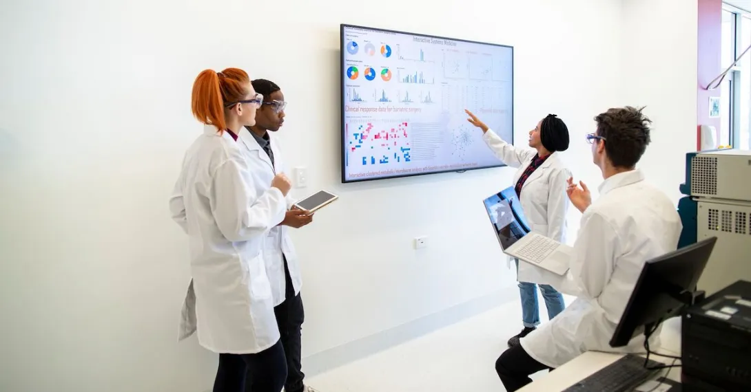 A group of researchers gathered around a screen displaying charts and data.