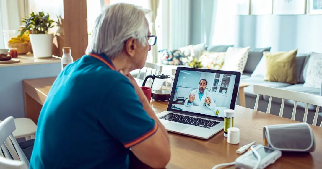A man talking to a doctor via a laptop with connected devices like a blood pressure cuff and a thermometer