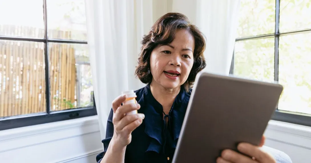 Person holding a tablet in one hand and a prescription bottle in the other