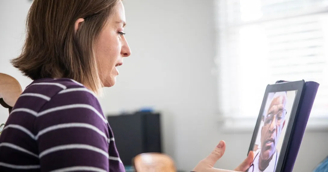 Person sitting down while looking at a computer with a telehealth provider on the screen