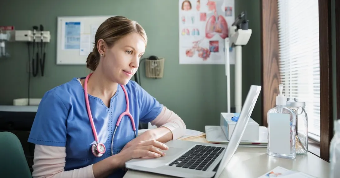 Healthcare provider in scrubs sitting at a desk and looking at a computer
