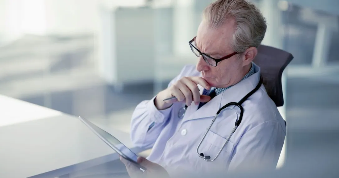 Healthcare provider looking at a tablet while holding their chin as though deep in thought